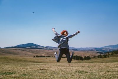 Full length of woman jumping on field against sky