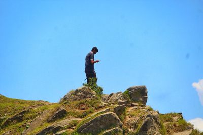 Man standing on rock against blue sky