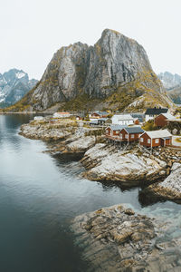 Houses at riverbank by rocky mountains against clear sky