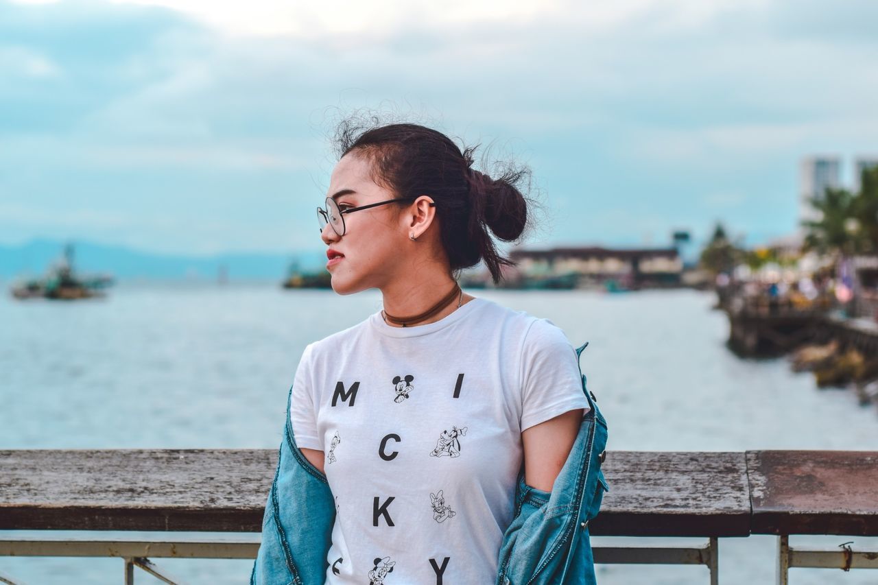 glasses, child, water, real people, focus on foreground, front view, standing, sky, lifestyles, boys, one person, childhood, casual clothing, nature, portrait, day, waist up, railing, outdoors, teenager, teenage boys, adolescence