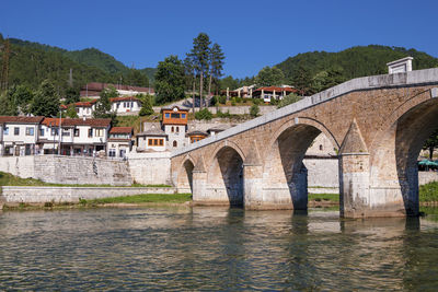 Arch bridge over river by buildings against clear sky