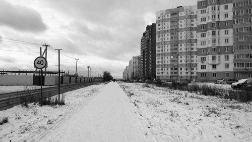 Snow covered road amidst buildings against sky