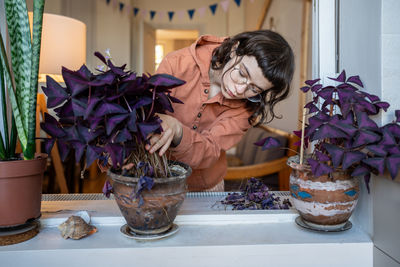 Concentrated florist teenager examining oxalis, tearing away dry leaves, taking care of plant