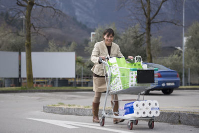 Portrait of happy woman pushing shopping cart at parking lot