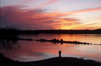 Silhouette woman standing by river against sky during sunset
