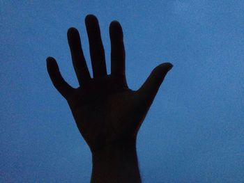 Low angle view of silhouette hand against clear blue sky