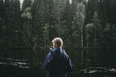 Rear view of boy looking away while standing by lake against trees