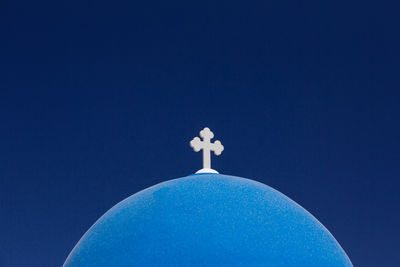 Low angle view of cross sculpture against blue sky