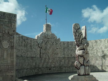 Sculpture by historic surrounding wall against sky