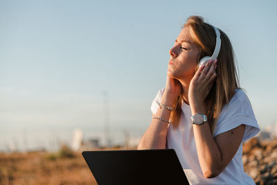 Young woman looking away while using smart phone against sky