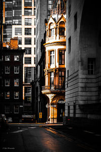 Illuminated street by buildings in city at night