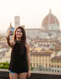 Portrait of smiling young woman using mobile phone in city