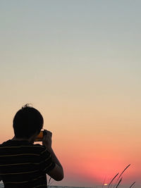 Rear view of a man standing against sky during sunset