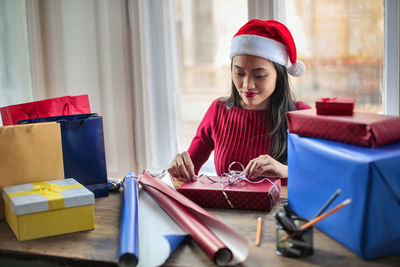 Young woman packing gift on table at home