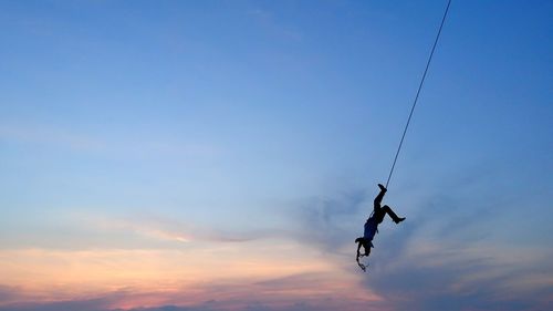 Low angle view of silhouette man hanging on rope against sky