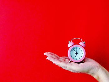 Close-up of hand holding clock against red background
