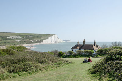 Two people staring at scenic view of field against clear sky with a beach house in the background 