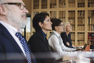 Concentrated lawyers listening in meeting while sitting at library