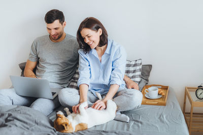 Couple with dog on bed against wall at home