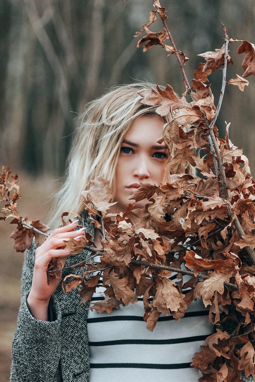 PORTRAIT OF YOUNG WOMAN WITH DRY LEAVES ON TREE