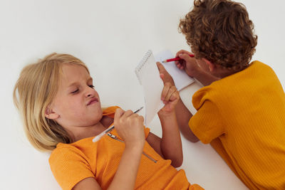 Sibling writing in notepad on white background