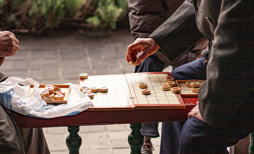 People sitting on table playing a traditional board game with wooden counters.