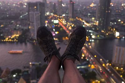 Low section of person over illuminated cityscape at dusk