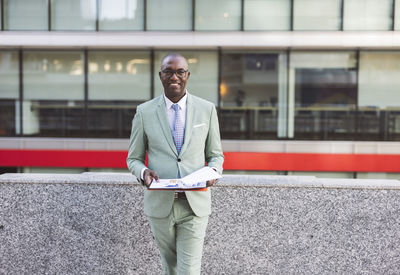 Happy businessman with documents standing in front of building