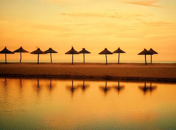 Silhouette parasols at beach against sky during sunset