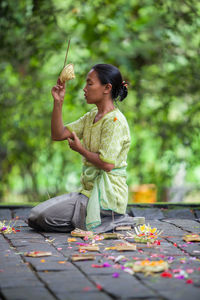 Side view of woman holding food while sitting on plant