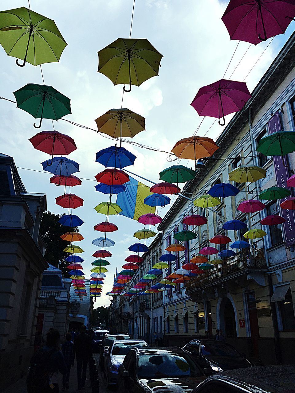 MULTI COLORED UMBRELLAS HANGING OVER STREET IN CITY