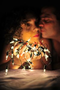 Close-up of illuminated string light against couple in darkroom