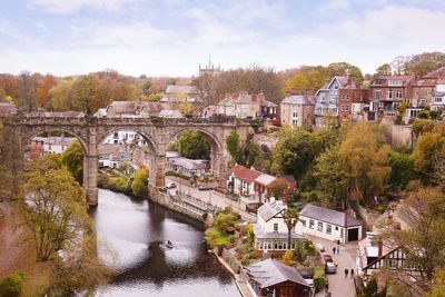 Bridge over river by buildings in city against sky