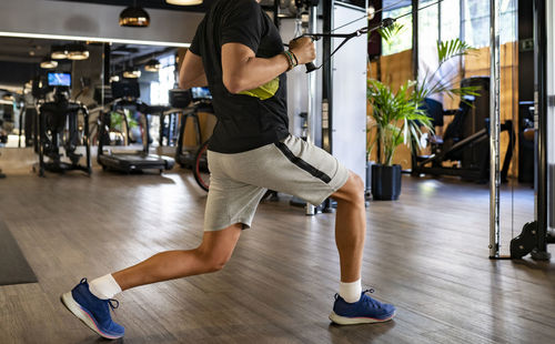 Side view of strong male lifting heavy weights on exercise machine while standing in lunge posture