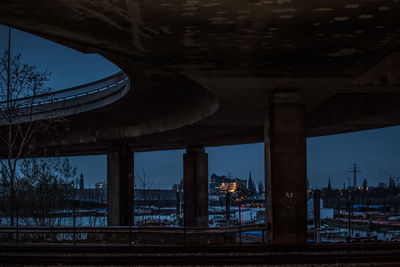 Illuminated bridge over river by buildings against sky at dusk