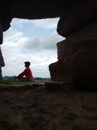 Man sitting on rock by sea against sky