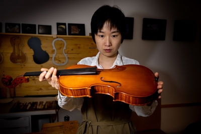 Young chinese woman violin maker checking the quality of her violin in the workshop