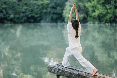 Yoga by the lake. young woman practicing warrior 1 pose or virabhadrasana i