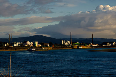 Sea by illuminated city against sky at sunset