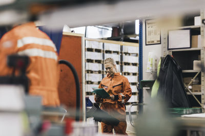 Young female worker examining file in factory warehouse