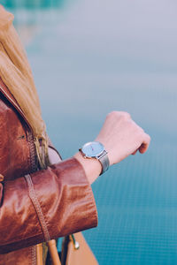 Midsection of woman checking time on wristwatch standing against blue wall