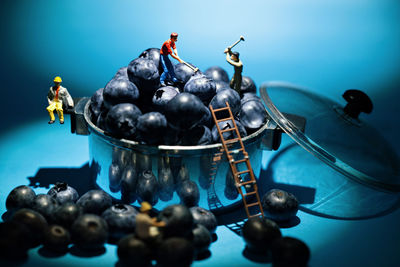 Close-up of figurines with blueberries in container against blue background