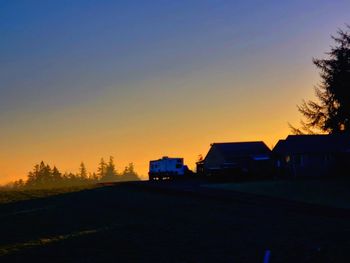 Road by silhouette buildings against sky during sunset