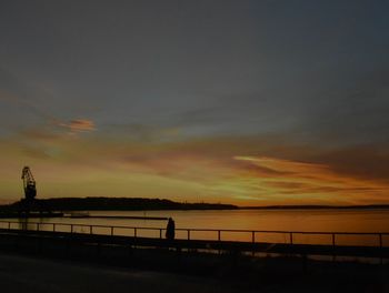 Silhouette bridge over sea against sky at sunset