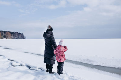 Woman and girl standing on snow covered landscape against sky