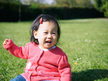 Portrait of cute girl sitting on grassy field during sunny day
