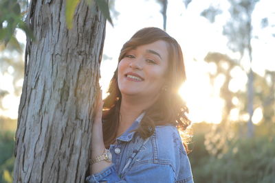 Portrait of smiling young woman against tree trunk