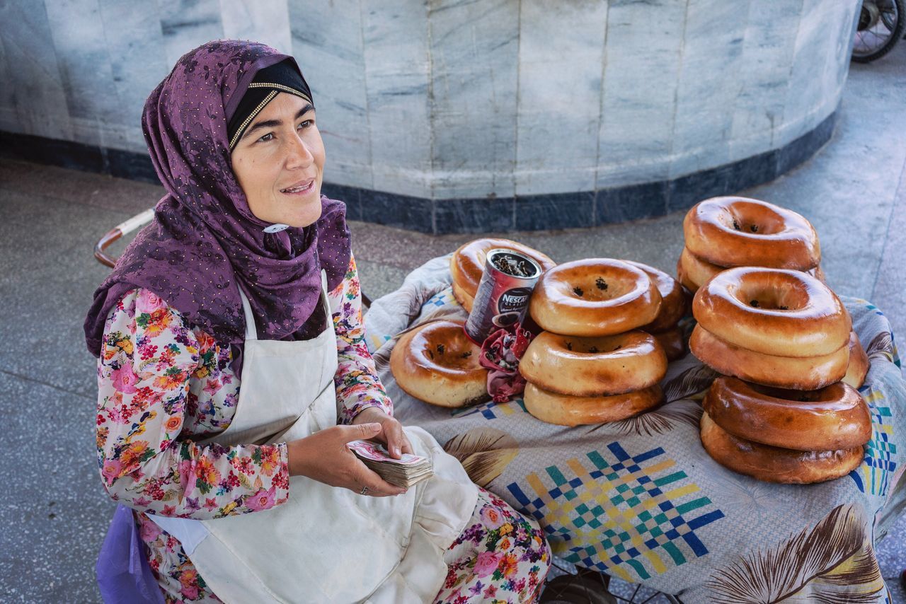 one person, real people, food and drink, leisure activity, sitting, lifestyles, clothing, food, day, women, sweet food, casual clothing, looking, headscarf, traditional clothing, young adult, freshness, sweet, temptation, outdoors, scarf