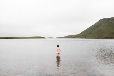 Naked man standing in lake against sky