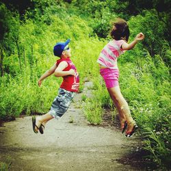 Brother and sister jumping against plants